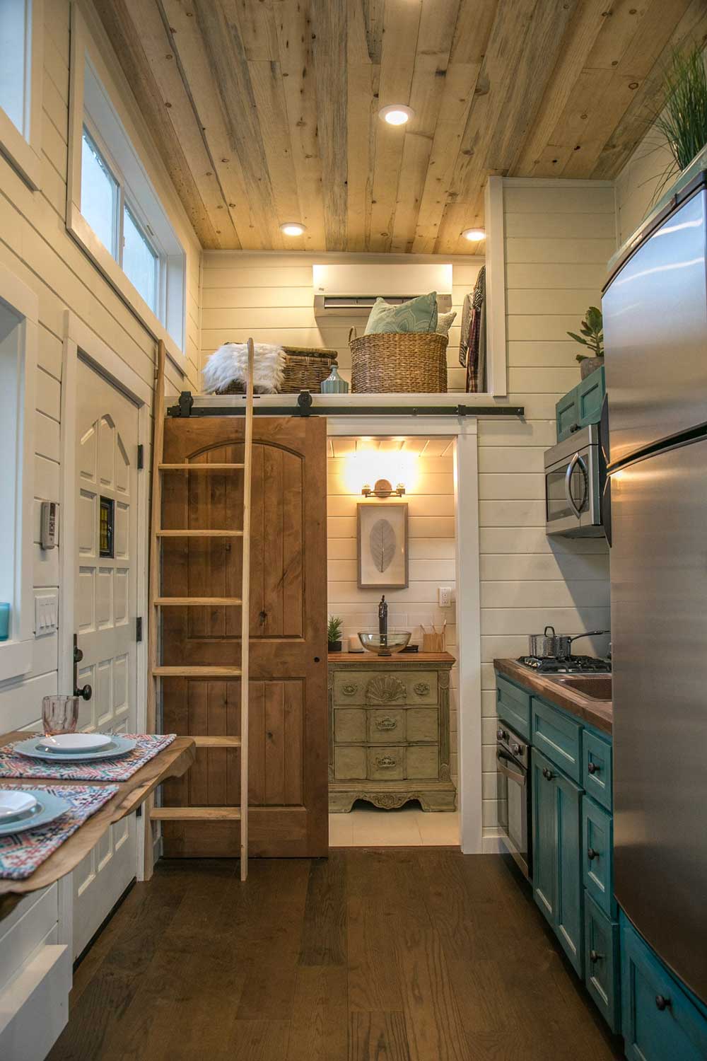 Interior of The Archway custom tiny house showing ladder and loft, bathroom, kitchen and dining counter