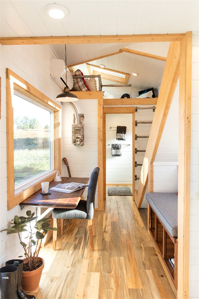 Interior of the Artists' Retreat custom tiny house showing big windows, a workl table, a loft and stairs to a second loft