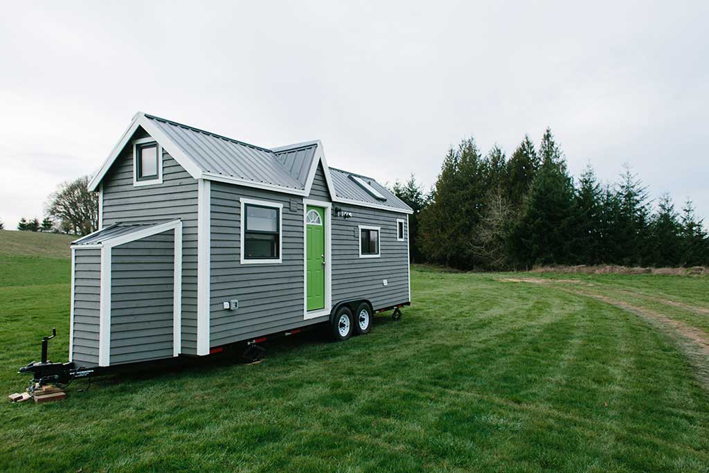 Outside view of The Emerald custom tiny house in a field with a forest in the background