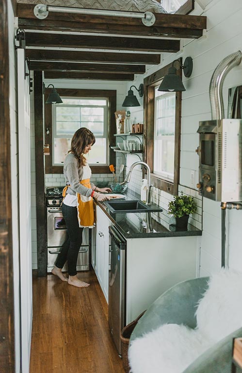 A woman cooks in the kitchen of the Tiny Heirloom Genesis custom tiny house