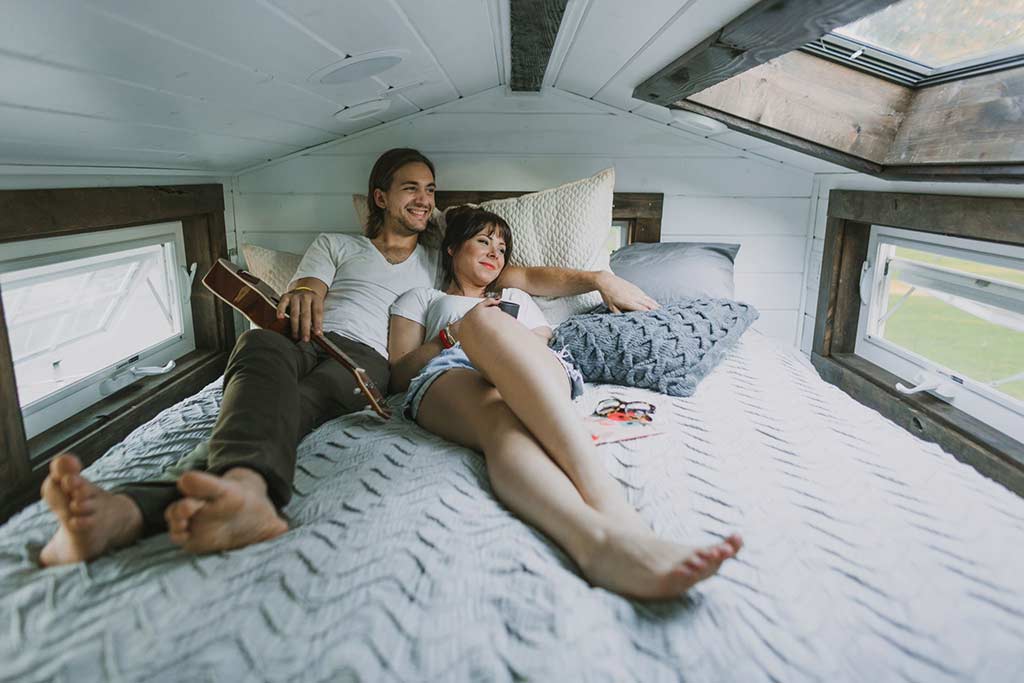 A couple lunges in the loft bedroom of their Tiny Heirloom Genesis custom tiny house