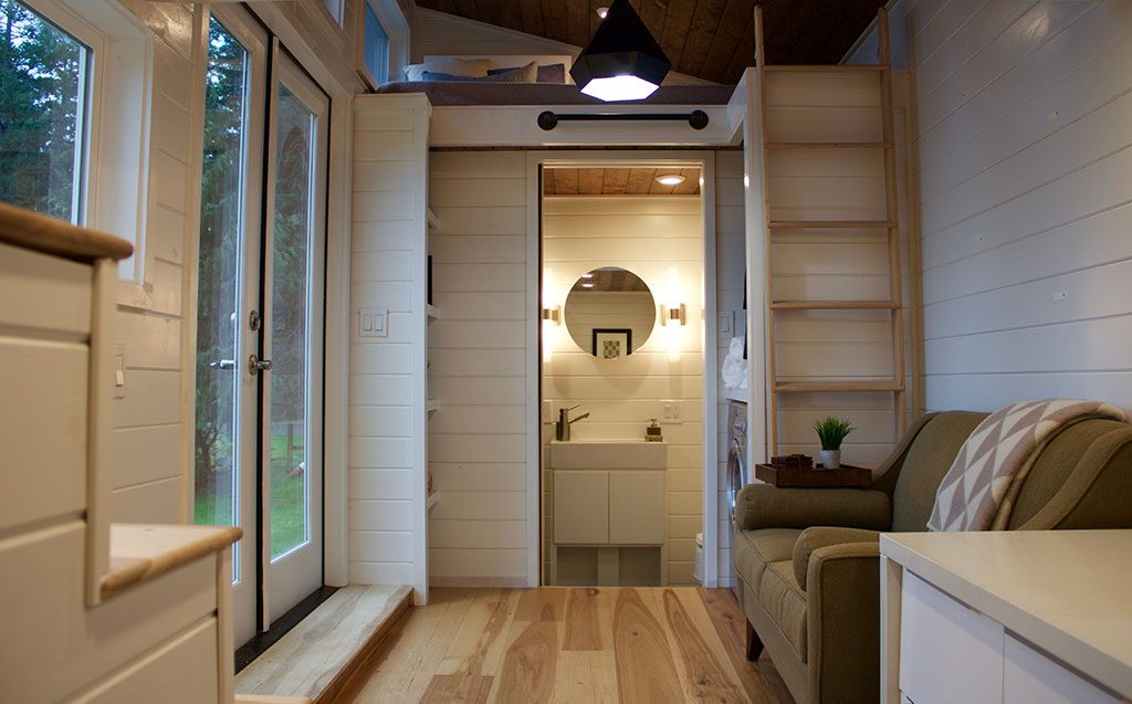 Interior of the Home Of Zen custom tiny house showing bathroom, ladder to loft and couch