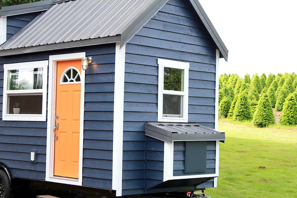 Outside shot of The Kalani custom tiny home showing orange door and blue siding