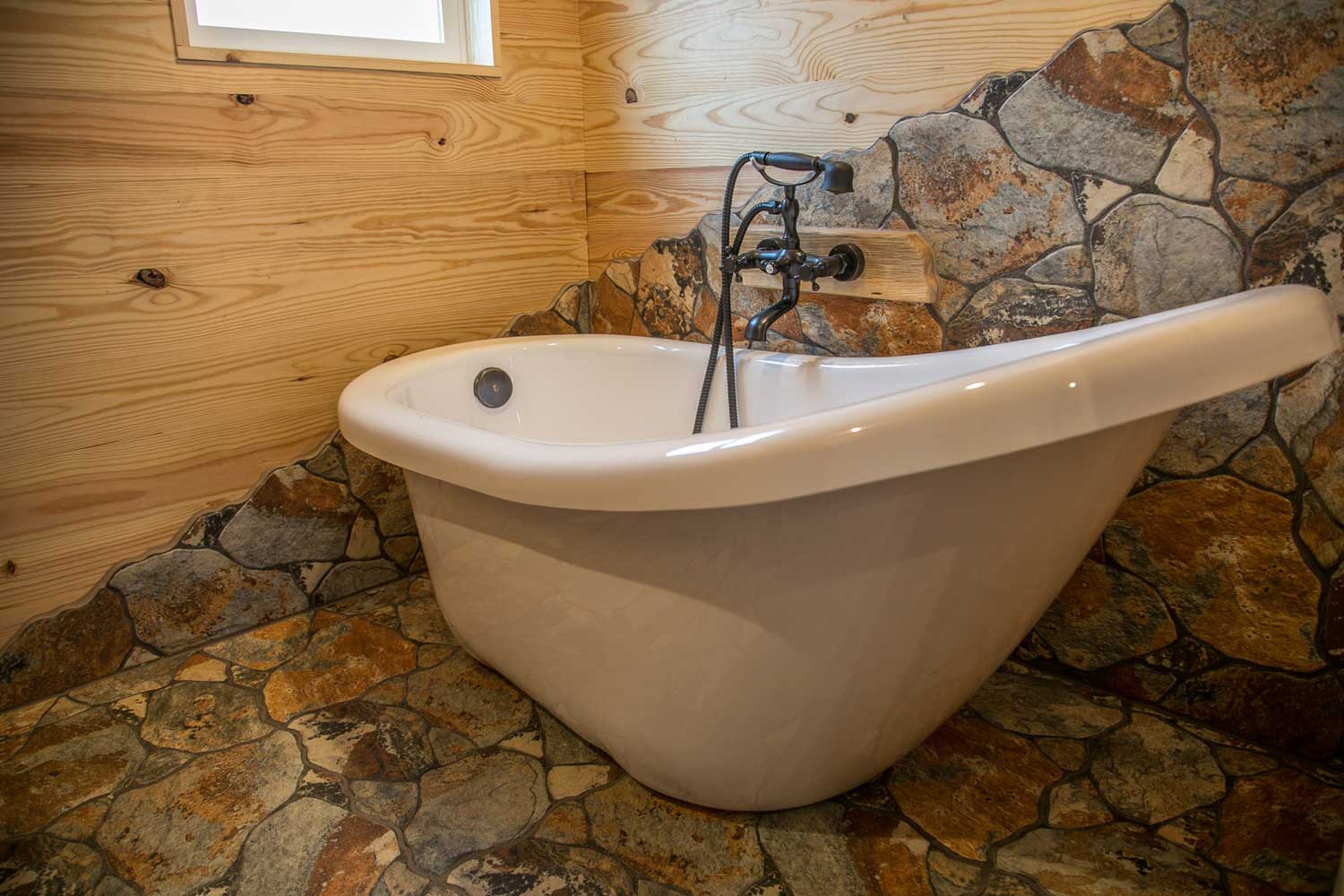 Bathtub with stonework floor and backsplash in the Rustic Mountaineer custom tiny house