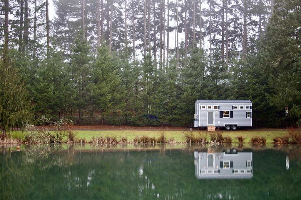 Far away shot of the Tiny Beach House custom tiny house refelctin in a lake