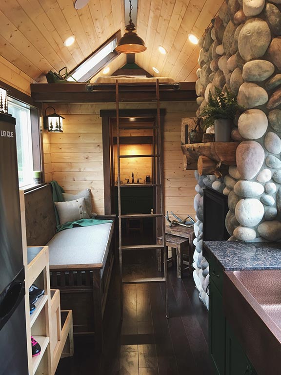Another interior shot of the Tiny Rustic Cabin custom tiny home showing a fireplace and couch