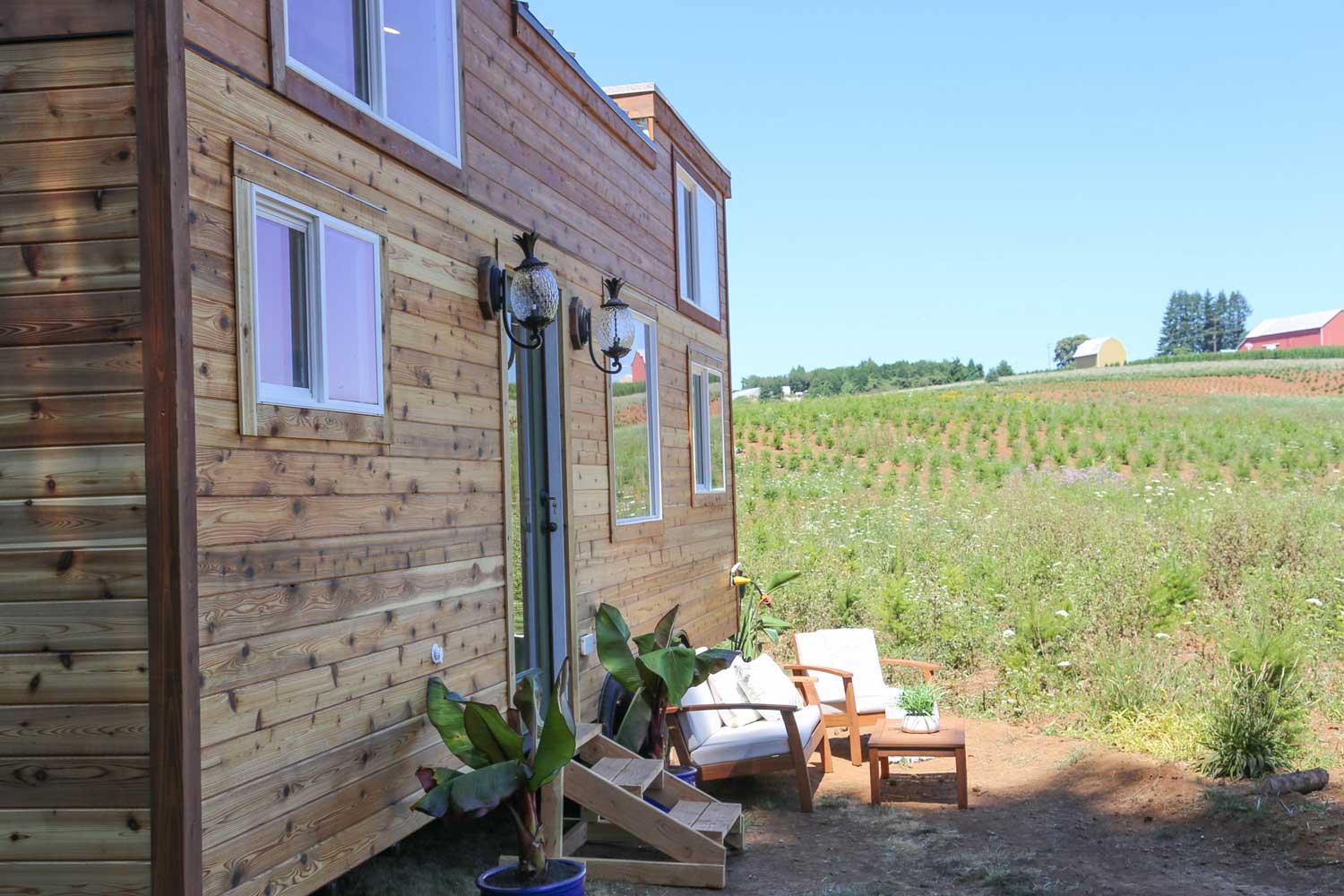 Outside of the Tropical Getaway custom tiny house with patio furniture, and a vineyard in the background