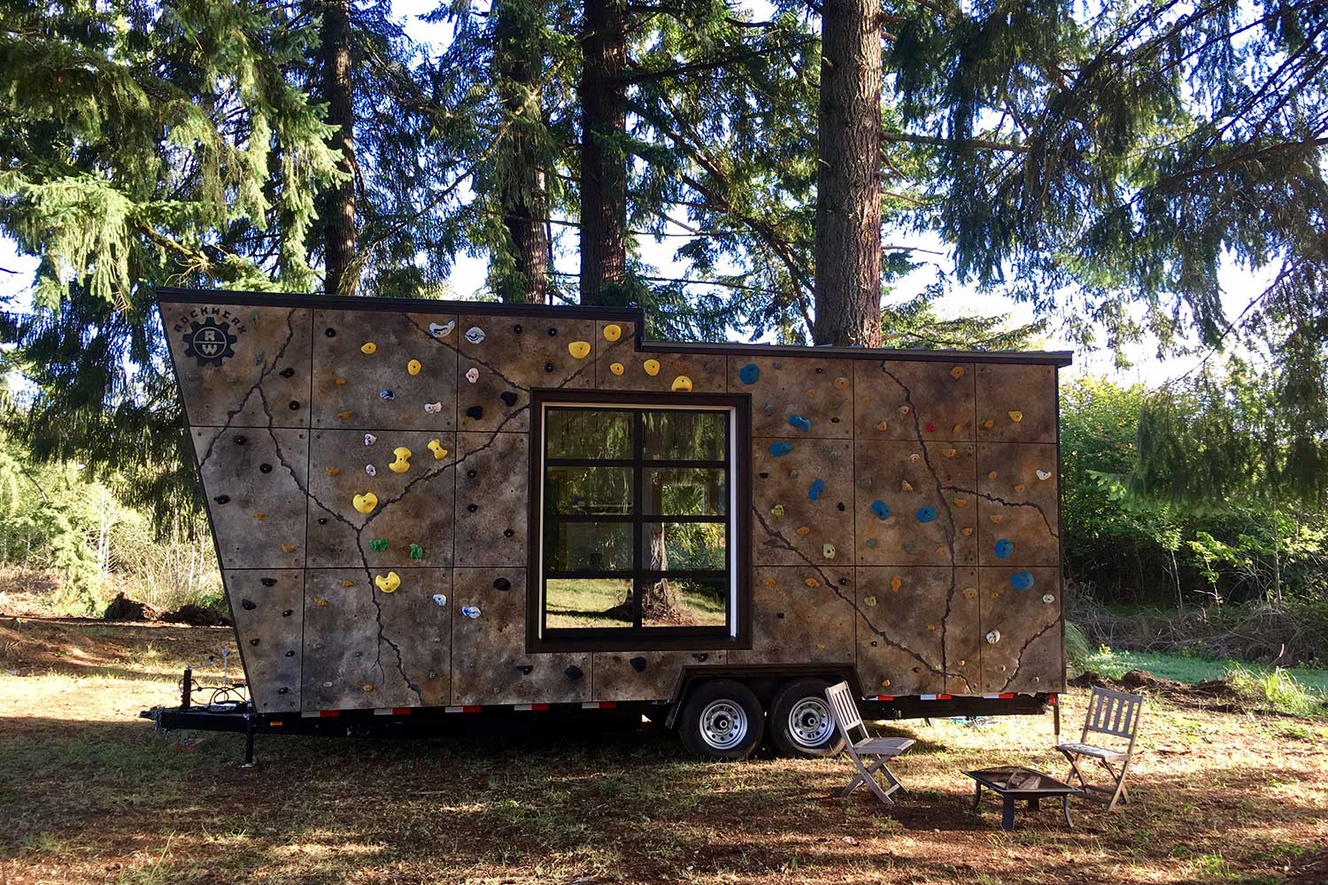 Exterior of fun custom tiny home with a climbing wall on the exterior, in a forested setting