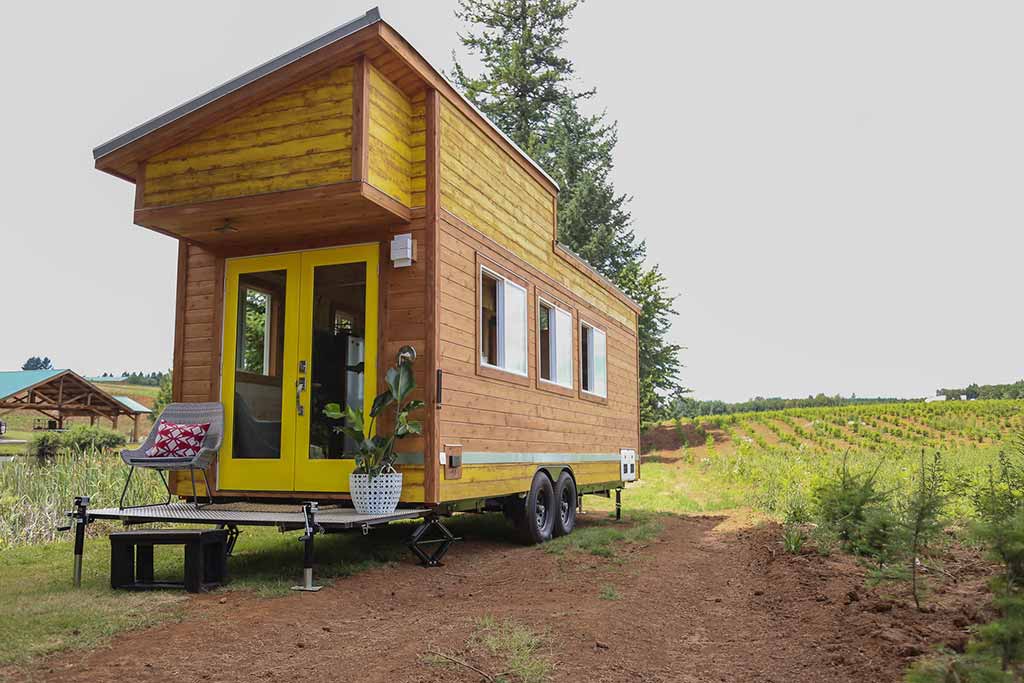 Outside of the Beachy Bohemian custom tiny home with a field and tree in the background
