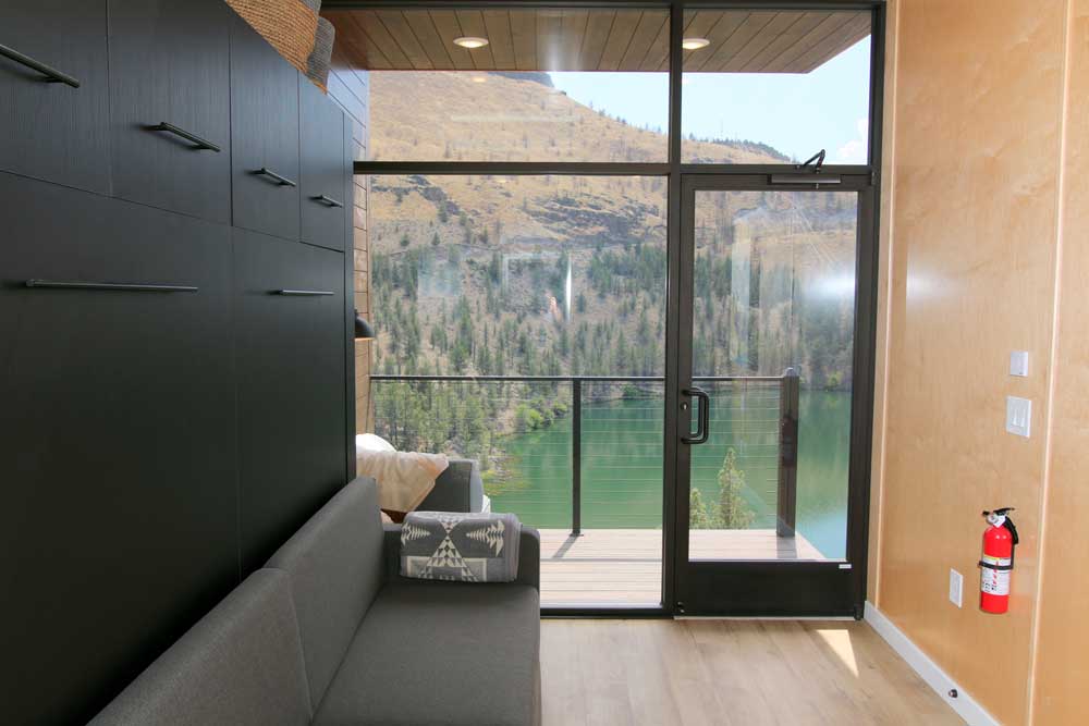 Interior of expanse tiny house used in a tiny house hotel in Oregon, with a view out big windows to a beautiful lake and hillside