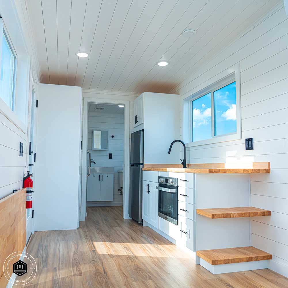 Interior of Legacy tiny house showing kitchen and bathroom with blue sky out the window