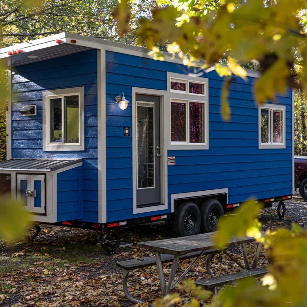Outside view of the True Blue custom tiny home set in a leafy forest
